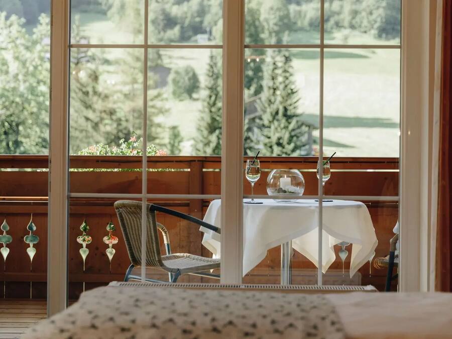 Ein Balkon mit Tisch für zwei, einem Korbstuhl und Blick auf eine grüne Landschaft.