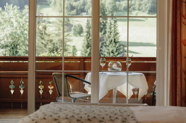 A balcony with a table set for two, a wicker chair, and a view of a green landscape. - Hotel Hirschen (Silbertal)