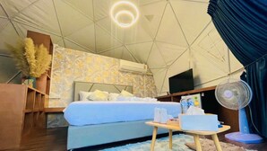 A tent-style room with a bed, a fan, a table with items, and a TV. - papa q suite resorts (Roi Et)
