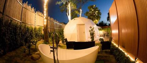 Un espace de bien-être comprenant une grande baignoire blanche, une petite structure en forme de dôme et une clôture en bois.
