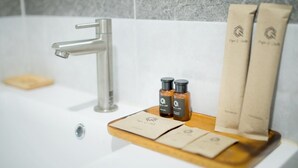 A bathroom with a modern faucet, two bottles of liquid soap, and two paper towels on a wooden tray. - papa q suite resorts (Roi Et)