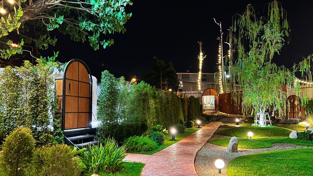 A well-lit pathway leading to a building with a large wooden door, surrounded by lush greenery and decorative lighting. - papa q suite resorts (Roi Et)