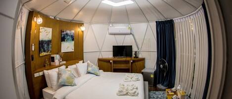 Habitación pequeña y bien iluminada con cama, mesita de noche y televisión.