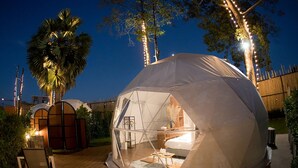 A dome-shaped tent with a bed, a table, and chairs inside, surrounded by a wooden deck and palm trees. - papa q suite resorts (Roi Et)