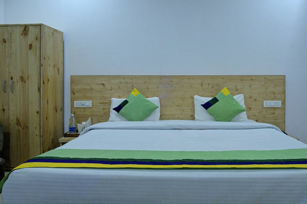 A hotel room with a wooden headboard, a bed with white bedding, and two pillows with geometric patterns.