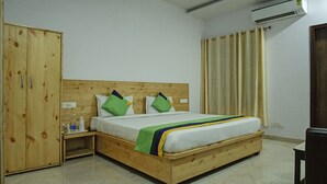A wooden bed with a headboard, a wooden wardrobe, a bedside table, and a curtain. - Treebo The King Mohali (Mohali)