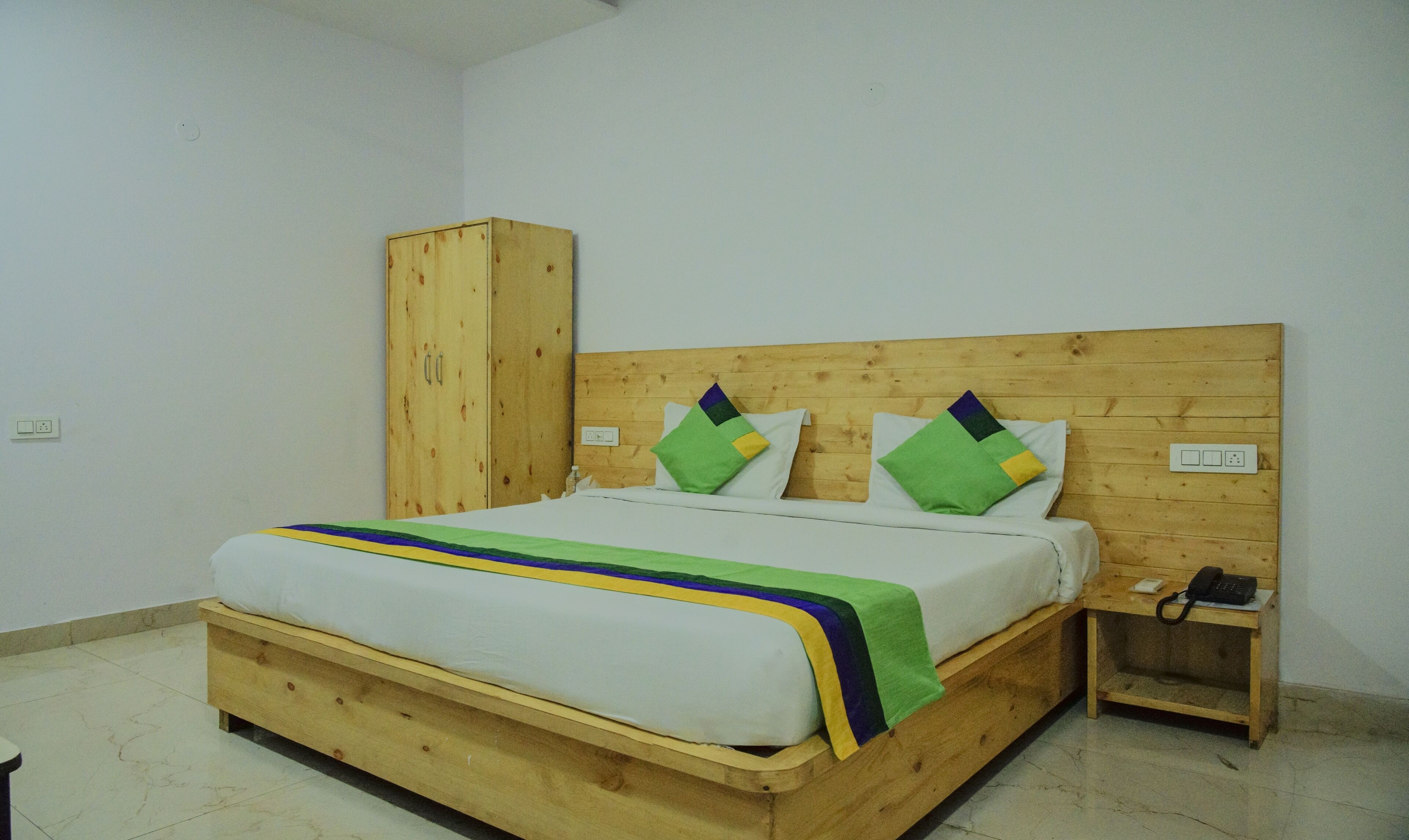 Uma cama de madeira com cabeceira, um guarda-roupa de madeira e uma mesa de cabeceira com telefone.
