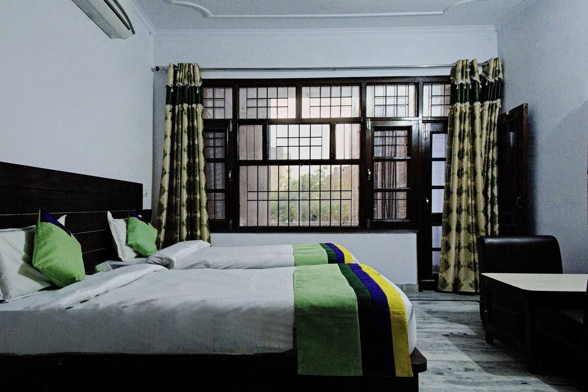 A hotel room with a bed, a chair, a window with curtains, and a radiator.
