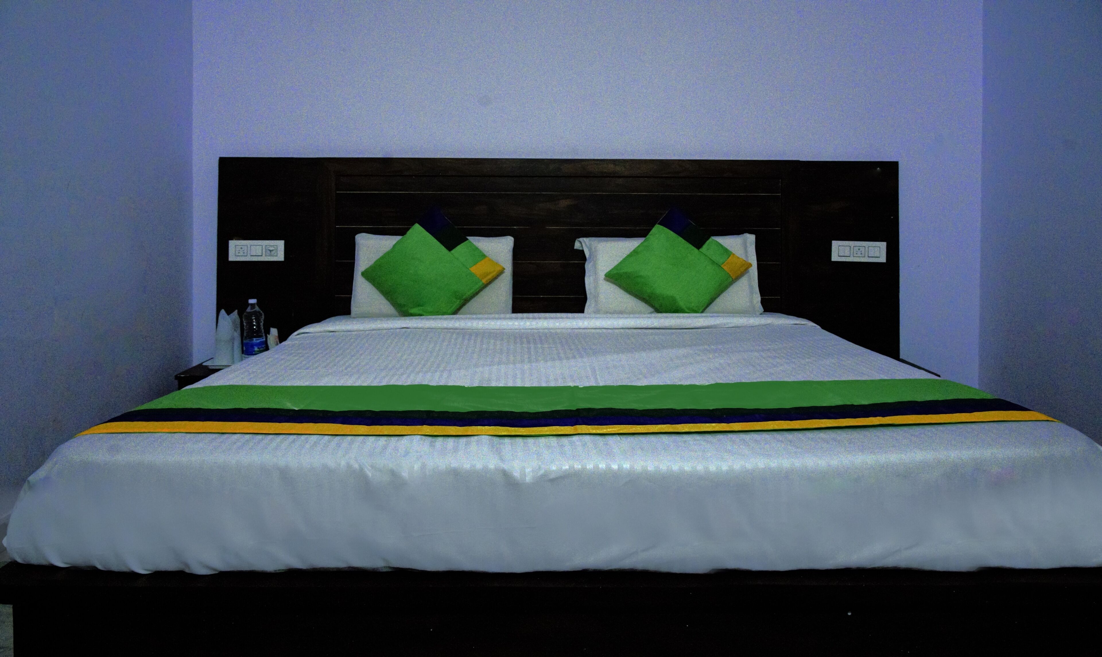 A bed with a white sheet, green pillows, and a striped bedspread.