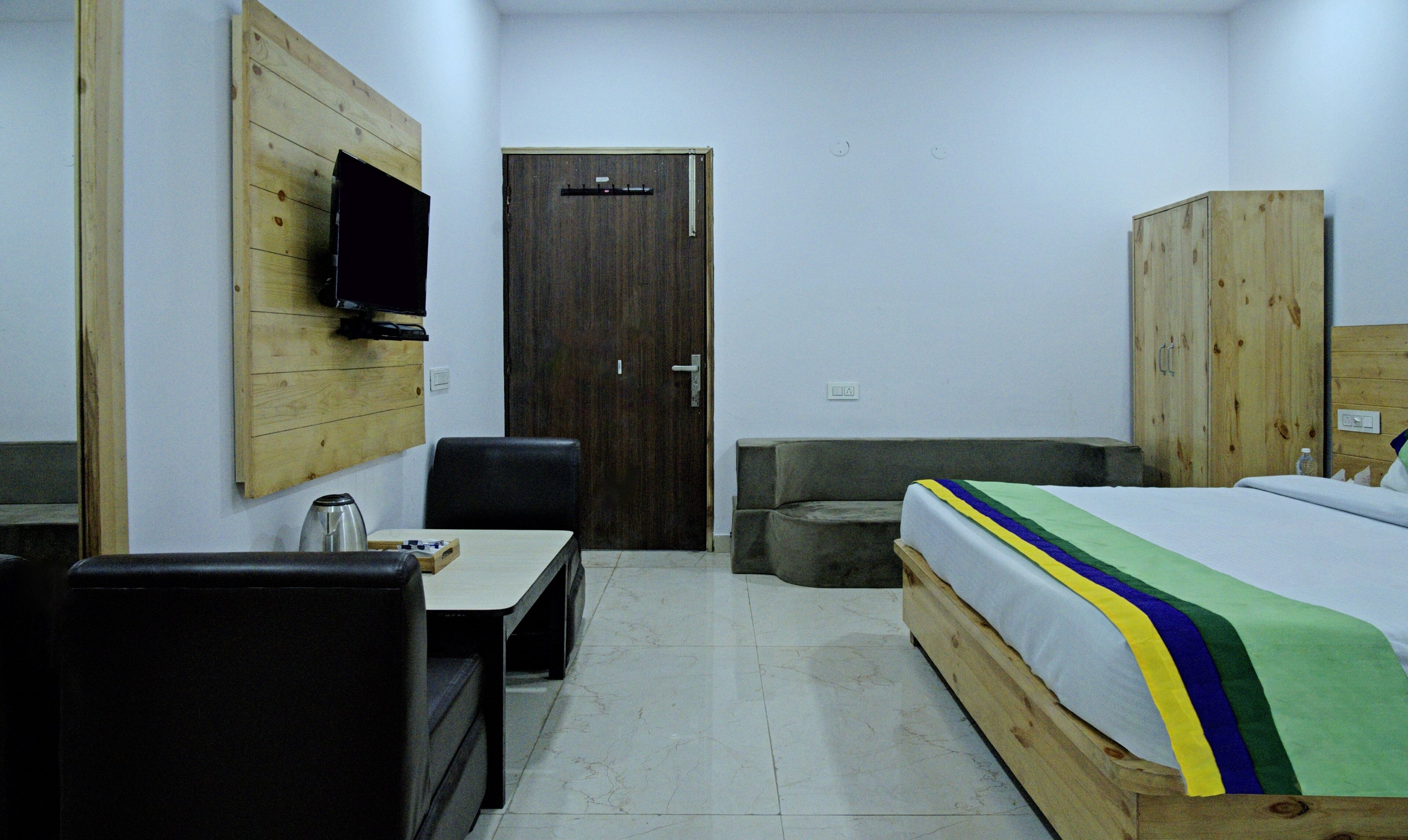 Habitación de hotel con un armario de madera, una cama con colcha colorida, un escritorio con silla y un televisor montado en la pared.