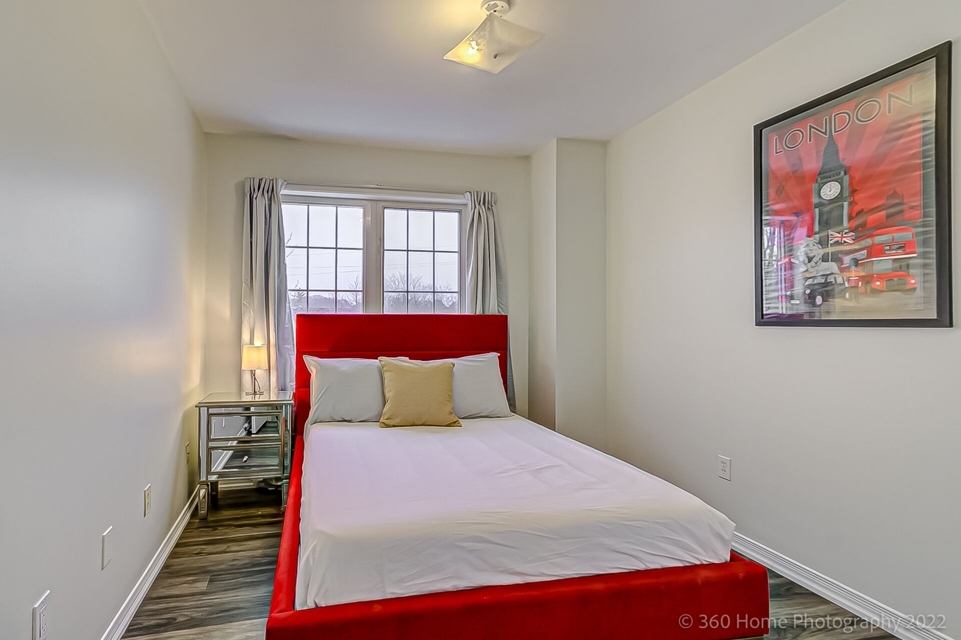 Une chambre à coucher avec une tête de lit rouge, un couvre-lit blanc et une fenêtre avec des rideaux.