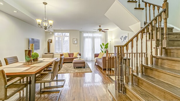 A spacious living room with a wooden dining table, comfortable seating, and a staircase with wooden railings. - Urban Retreat A Modern 5BR Townhouse (Toronto)