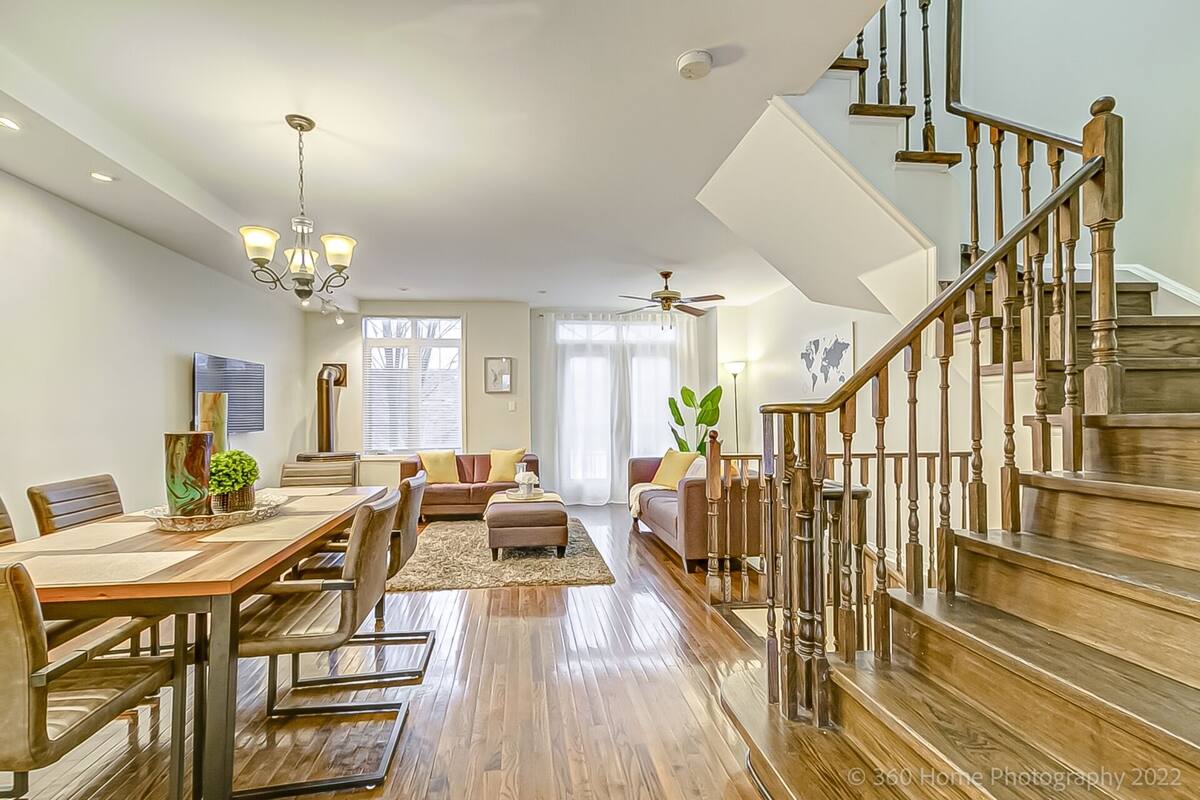 A spacious living room with a wooden dining table, comfortable seating, and a staircase with wooden railings.