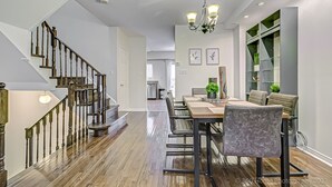 A modern dining area with a wooden table, chairs, and a chandelier. A staircase with wooden railings is visible on the left. - Urban Retreat A Modern 5BR Townhouse (Toronto)