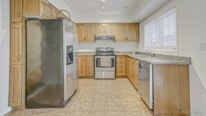 A kitchen with wooden cabinets, stainless steel appliances, and a window with blinds. - Urban Retreat A Modern 5BR Townhouse (Toronto)