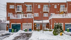 A multi-story brick apartment building with white railings on balconies, a garage, and a snow-covered driveway. - Urban Retreat A Modern 5BR Townhouse (Toronto)