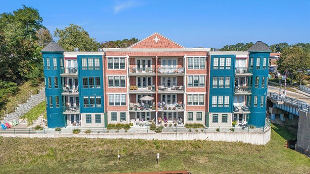 A multi-story building with balconies, a central courtyard, and a waterfront view. - 2 Bedroom River Front Condo (Manistee)
