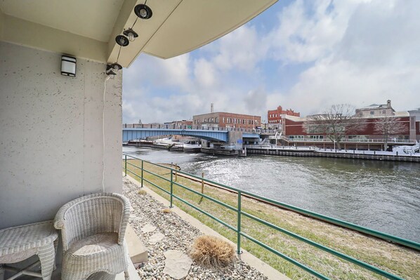 A balcony with wicker furniture, a view of a river, a bridge, and buildings in the background.