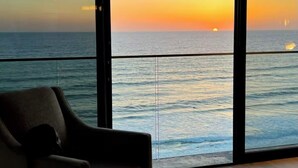 A room with a large window overlooking the ocean at sunset. - Ocean View Luxury Condo: Beachfront, and Pool (San Diego)