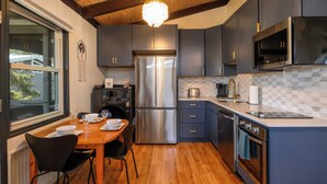 A modern kitchen with a stainless steel refrigerator, dark cabinets, and a wooden dining table. - Newly Updated OCEAN BLOCK 2 bedroom condo, steps away from the beach! (Dewey Beach)