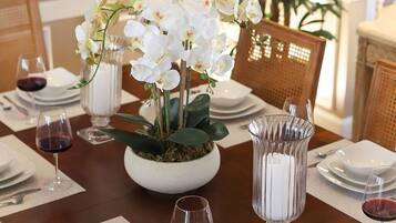 A dining table set with white plates, wine glasses, a bowl of croissants, a vase of white orchids, and a candle holder.
