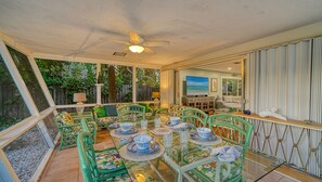 A dining area with a glass table, green chairs, and a ceiling fan.