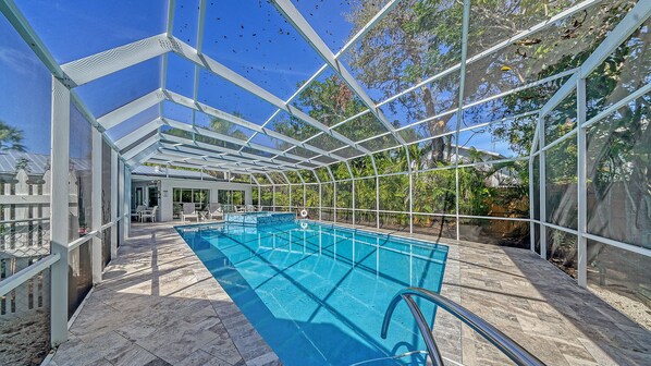 A covered swimming pool with a clear blue water, surrounded by a metal frame structure, and a patio area with chairs and tables.