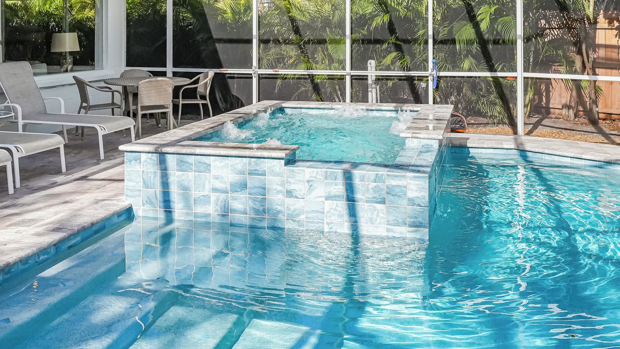 A swimming pool with a tiled edge and a hot tub area.