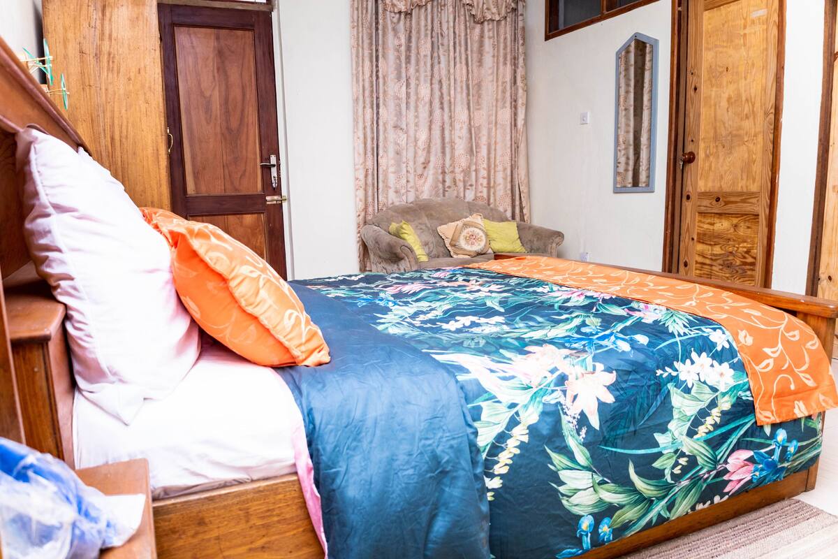 Ein Schlafzimmer mit einem hölzernen Bett, floraler Bettwäsche, einem Holzschrank und einem kleinen Stuhl.