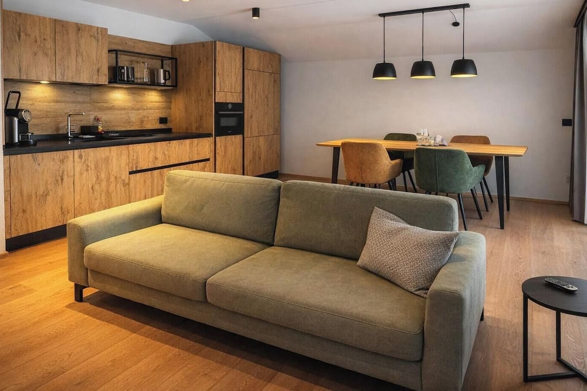 Un salon moderne comprenant un canapé, une table à manger avec des chaises et un coin cuisine doté de meubles et d’appareils électroménagers en bois.