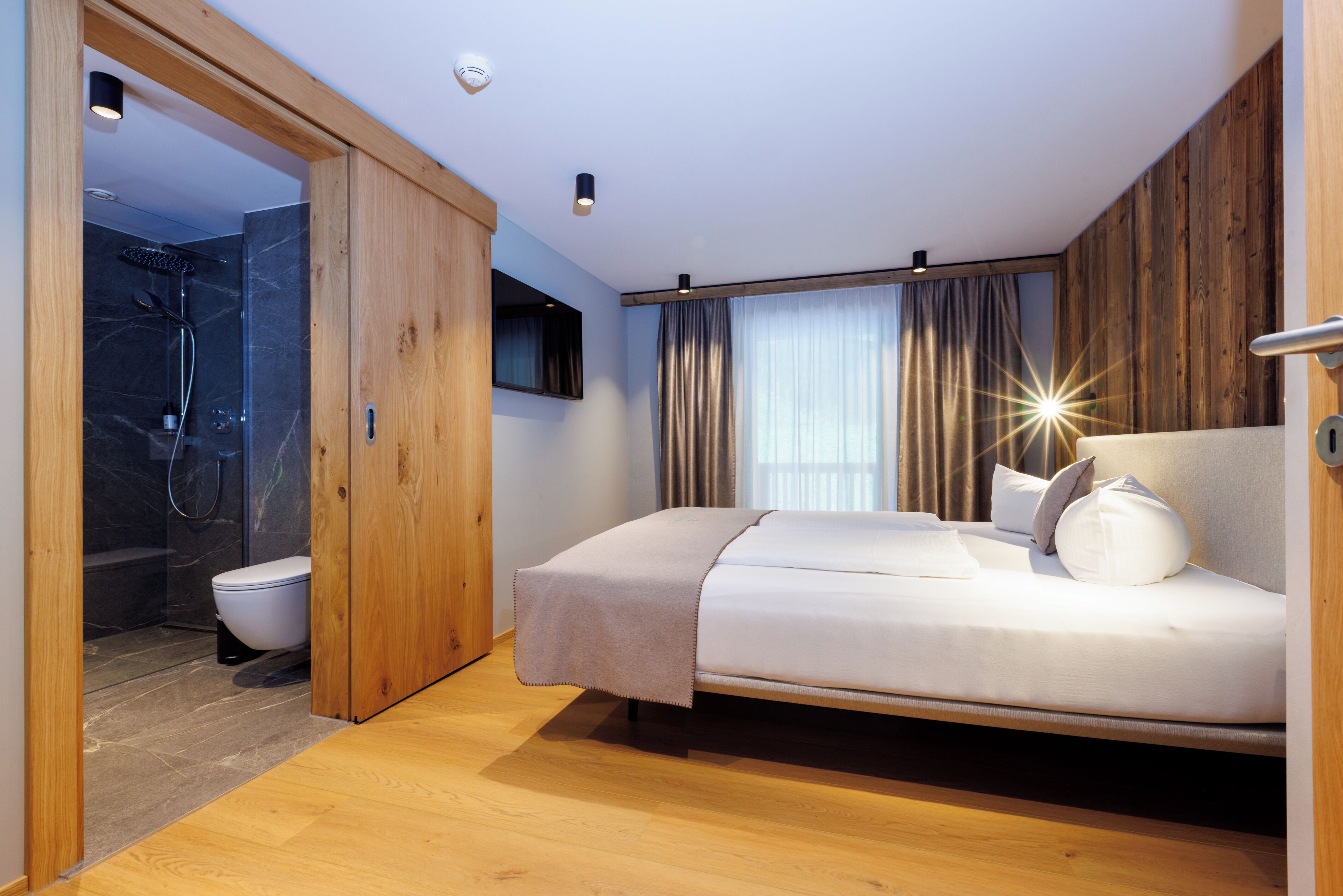 A modern bedroom with a wooden floor, a bed, a shower, and a toilet.