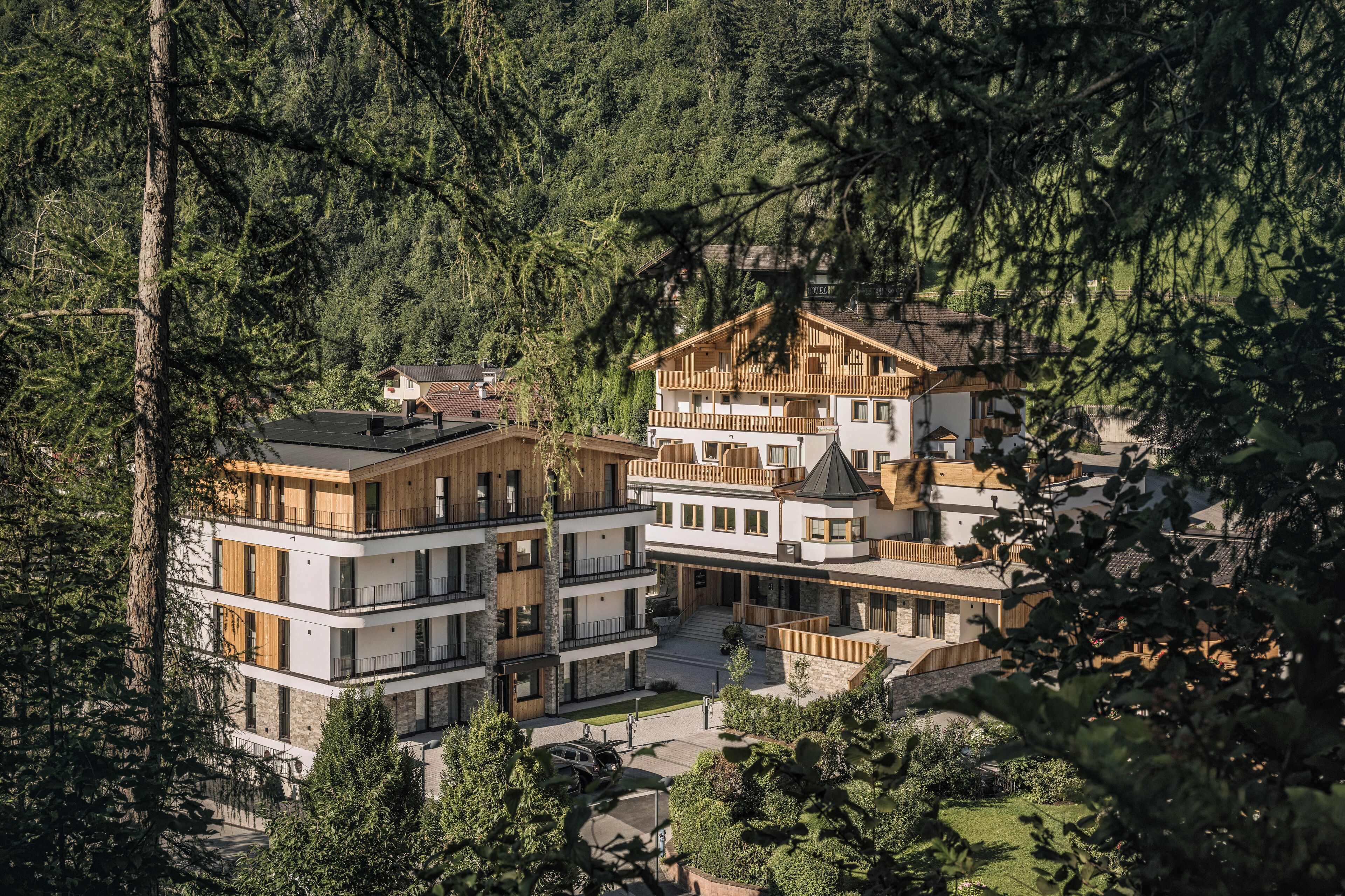 Un hotel de varios pisos con diseño moderno, rodeado de un bosque denso.