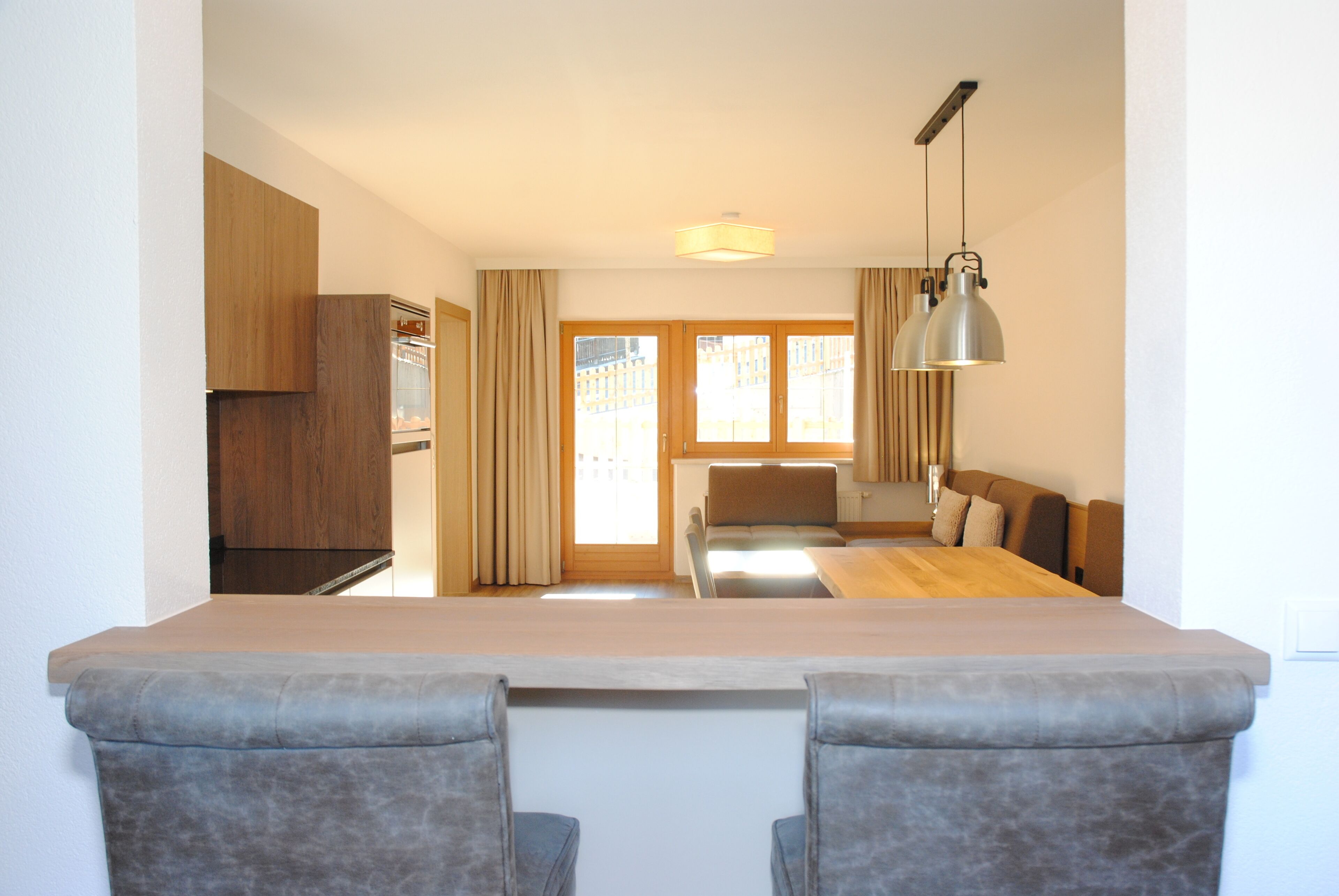 A modern kitchen with wooden cabinets, a dining area with a table and chairs, and a view of the city through large windows.