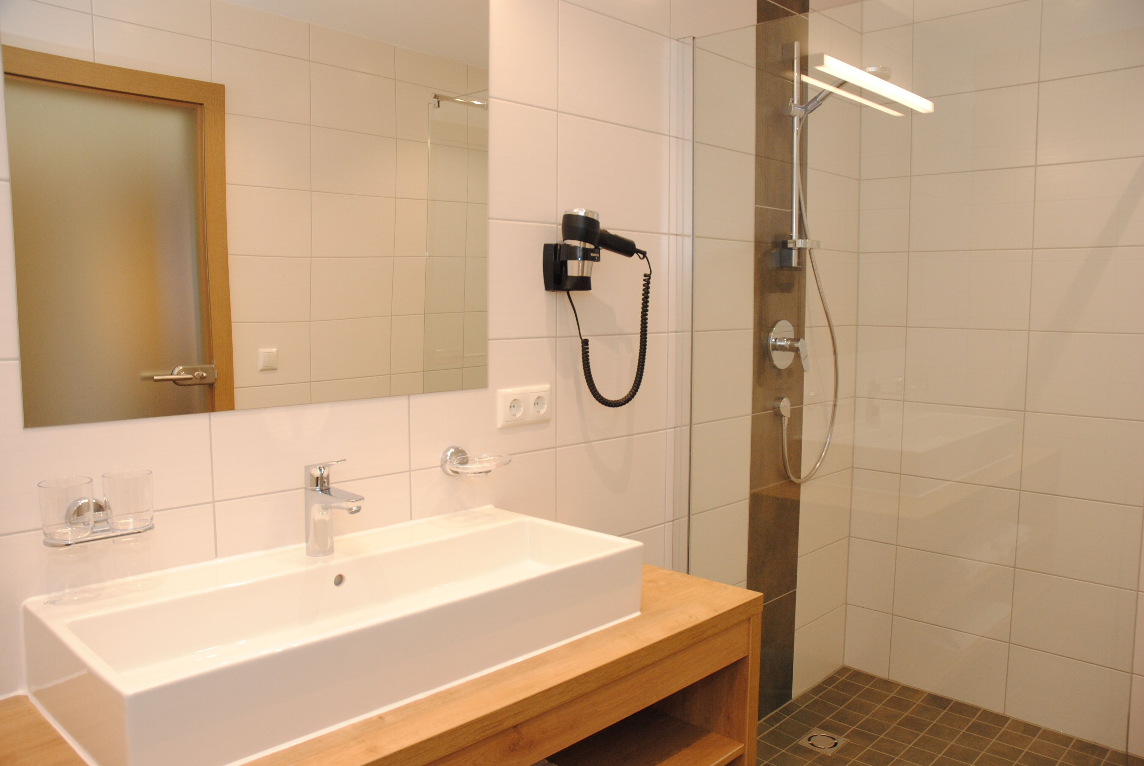 Une salle de bain moderne avec un grand lavabo blanc, un miroir et une douche séparée par des parois en verre.