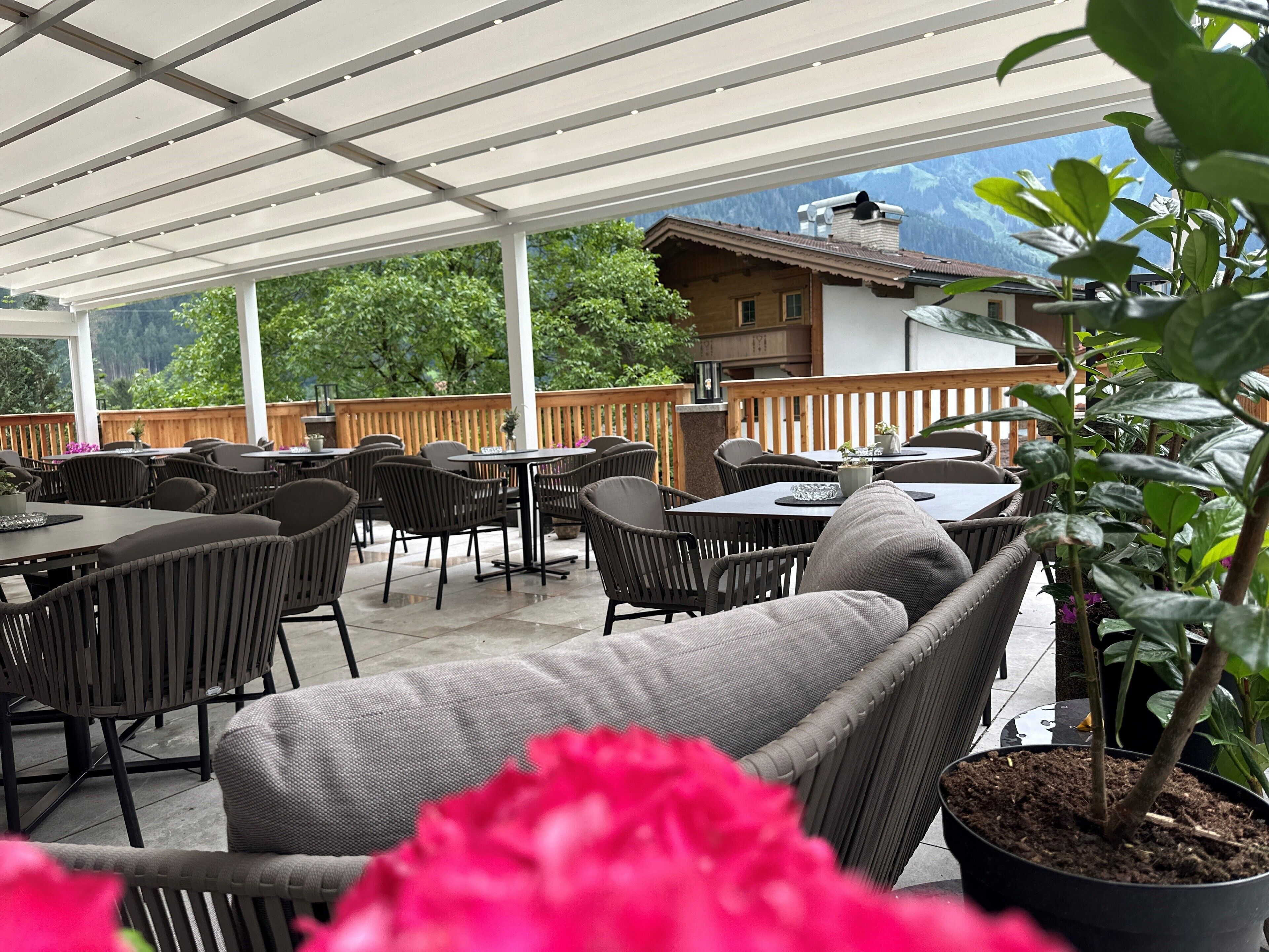 Un patio al aire libre con mesas y sillas, una terraza de madera y vistas a la montaña.