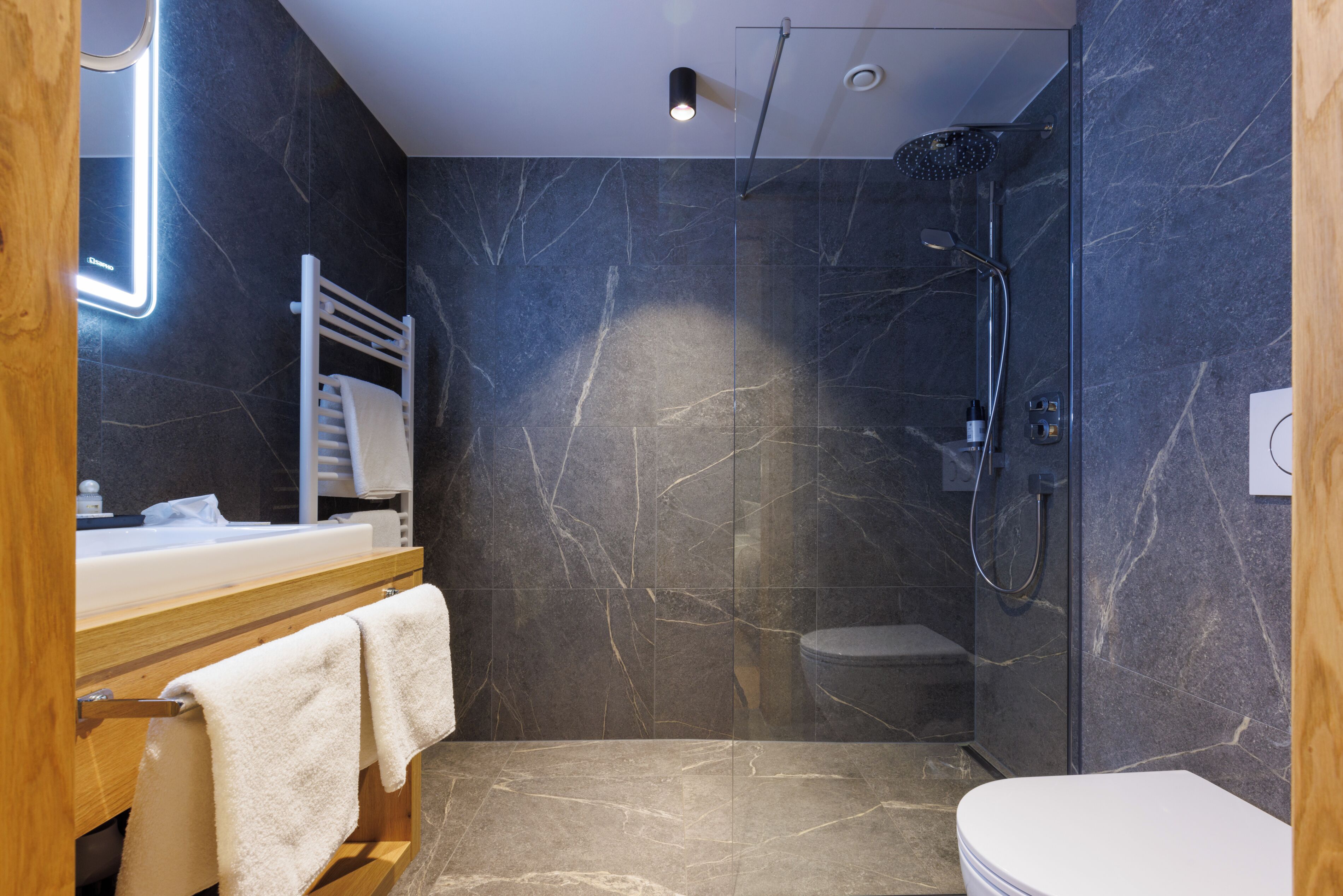 Un baño moderno con cabina de ducha de vidrio, inodoro blanco y tocador de madera con espejo.