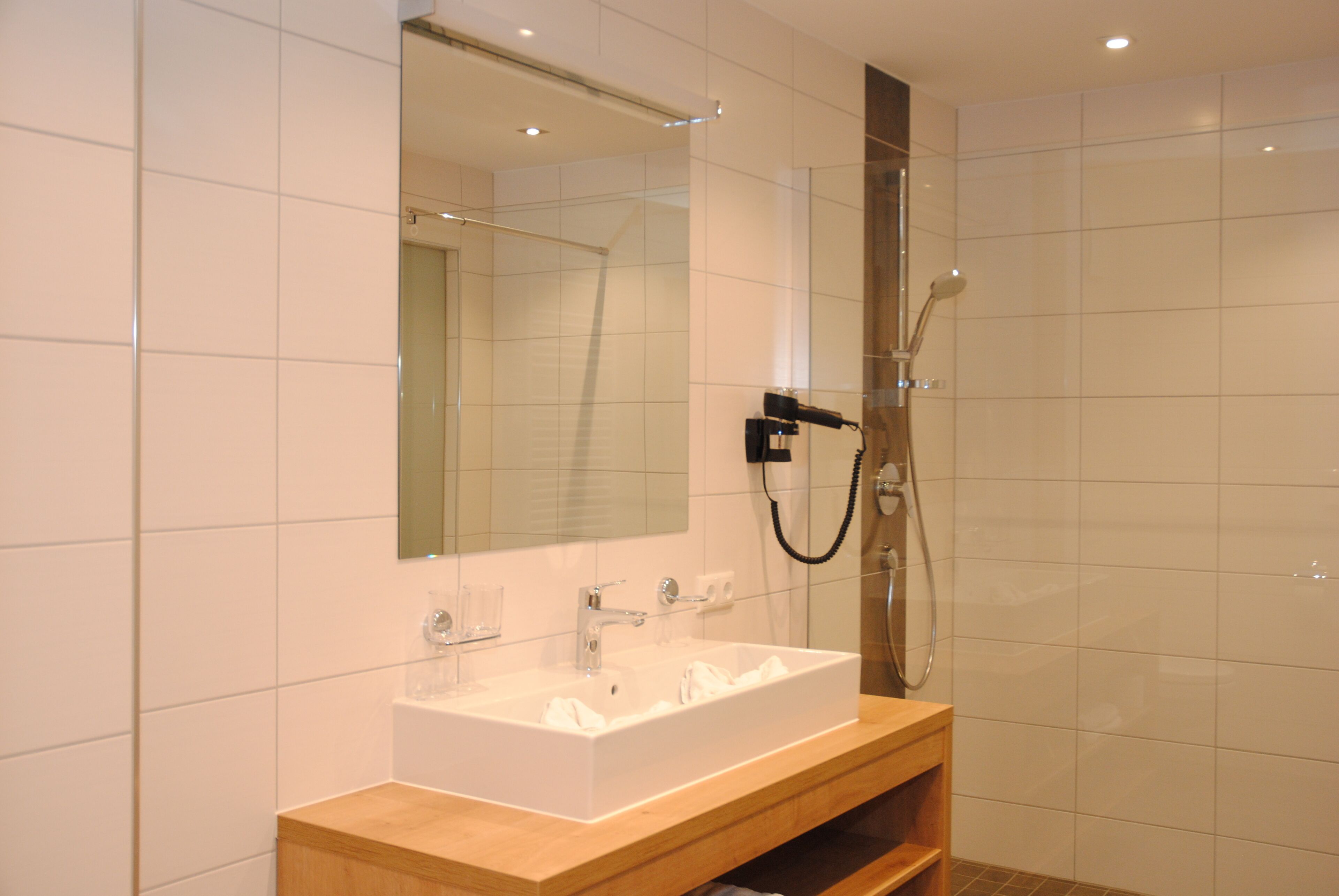 Une salle de bain moderne avec un grand miroir, un lavabo blanc et une douche.