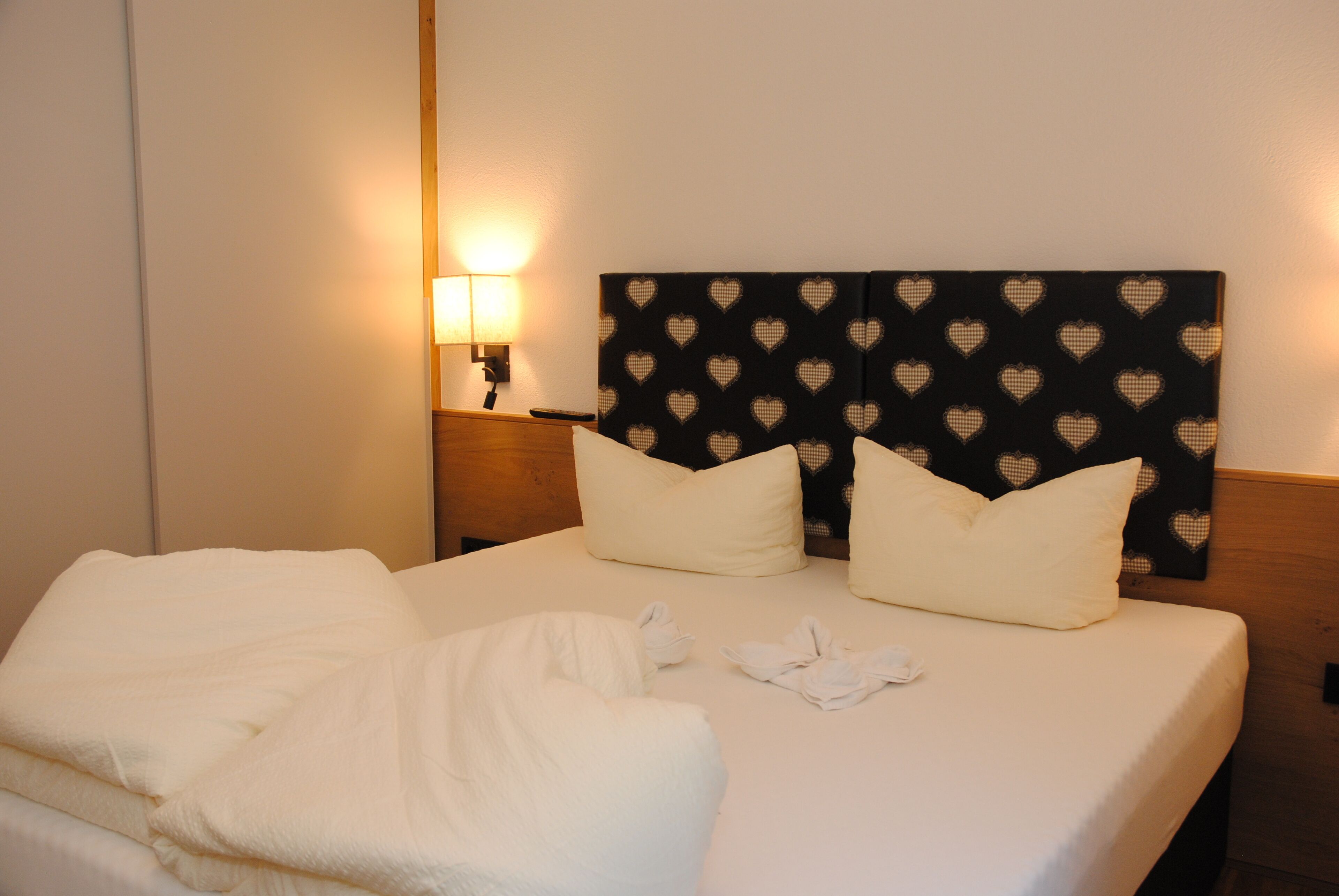 Een hotelkamer met een netjes opgemaakt bed, een hoofdbord met hartmotieven en een bedlamp.