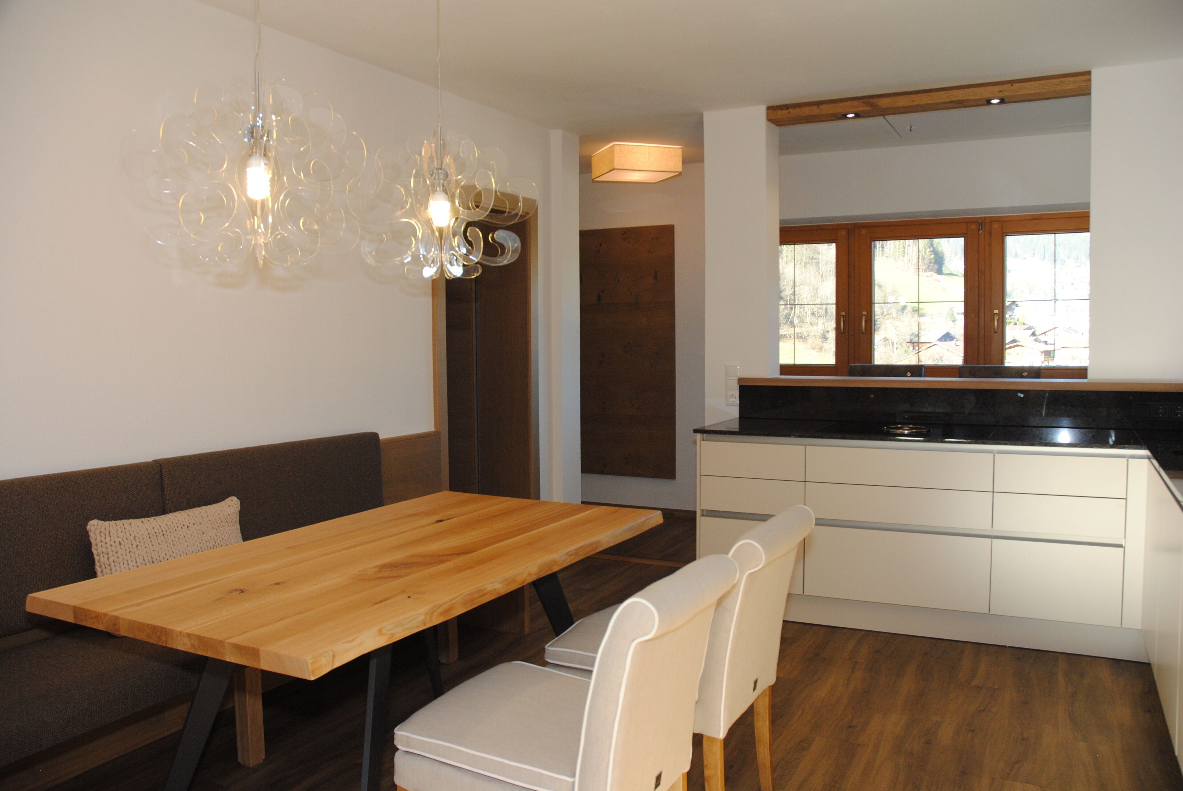 Eine moderne Küche mit Holzarbeitsplatte und weißen Schränken, ein Essbereich mit Holztisch und Stühlen sowie ein großes Fenster mit Blick ins Freie.