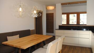 Eine moderne Küche mit Holzarbeitsplatte und weißen Schränken, ein Essbereich mit Holztisch und Stühlen sowie ein großes Fenster mit Blick ins Freie.