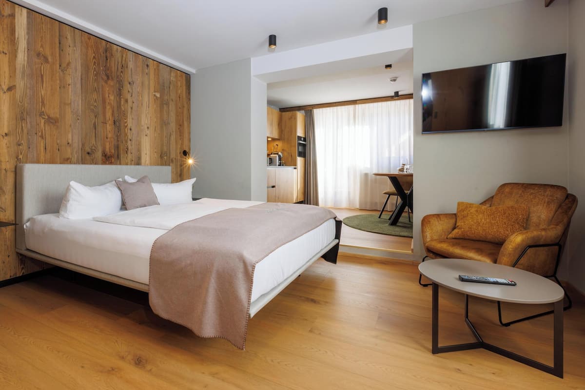 Une chambre d’hôtel moderne avec un mur d’accent en bois, un lit, une télévision, un canapé et une petite table.