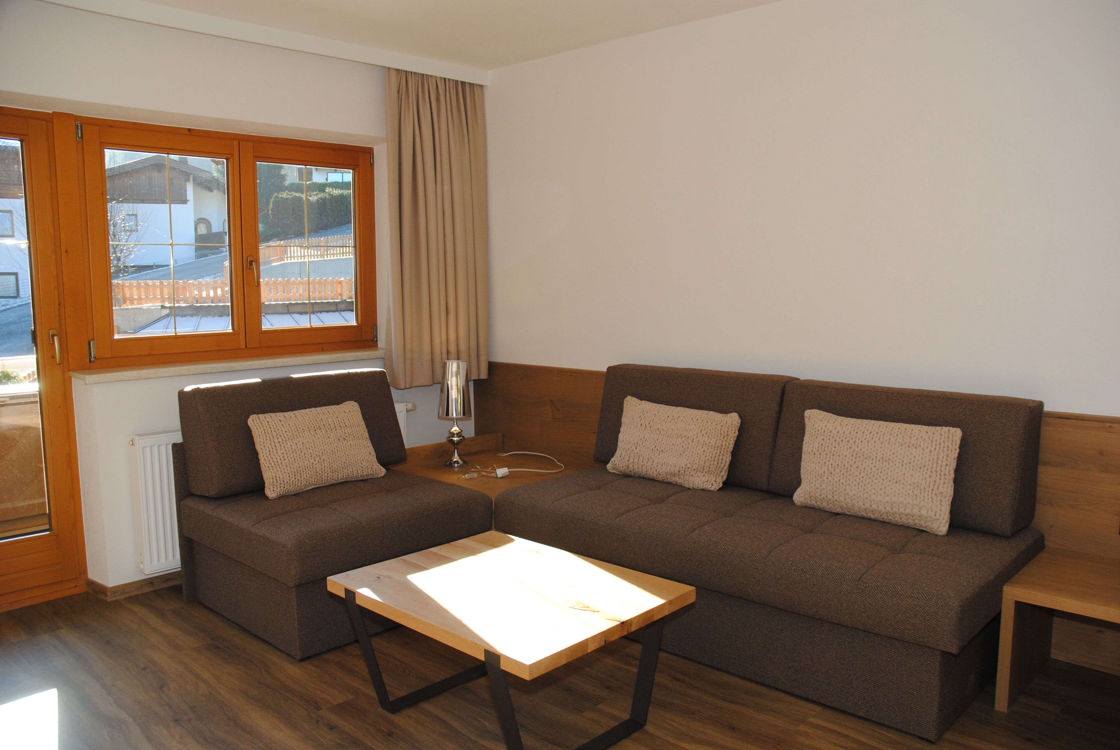 A living room with a brown sofa, a wooden coffee table, and a window with curtains.