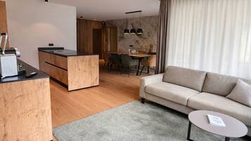 A modern living room with a sofa, a small round table, and a kitchen area with a wooden counter and dining table.