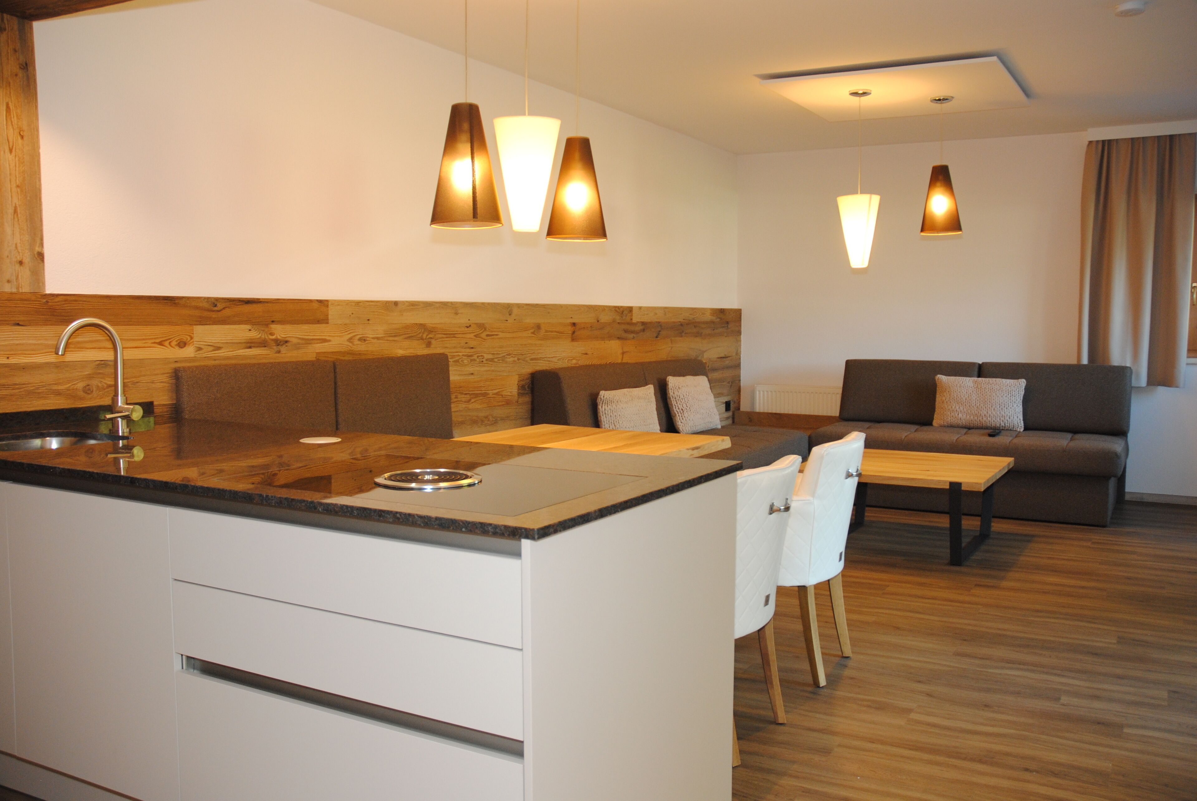 Una cocina moderna con una pared de acento de madera, un comedor con mesa y sillas blancas, y una sala de estar con sofá y mesa de centro.