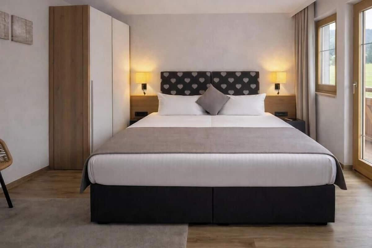Une chambre d’hôtel avec un grand lit, deux tables de chevet, une chaise et une vue sur l’extérieur.