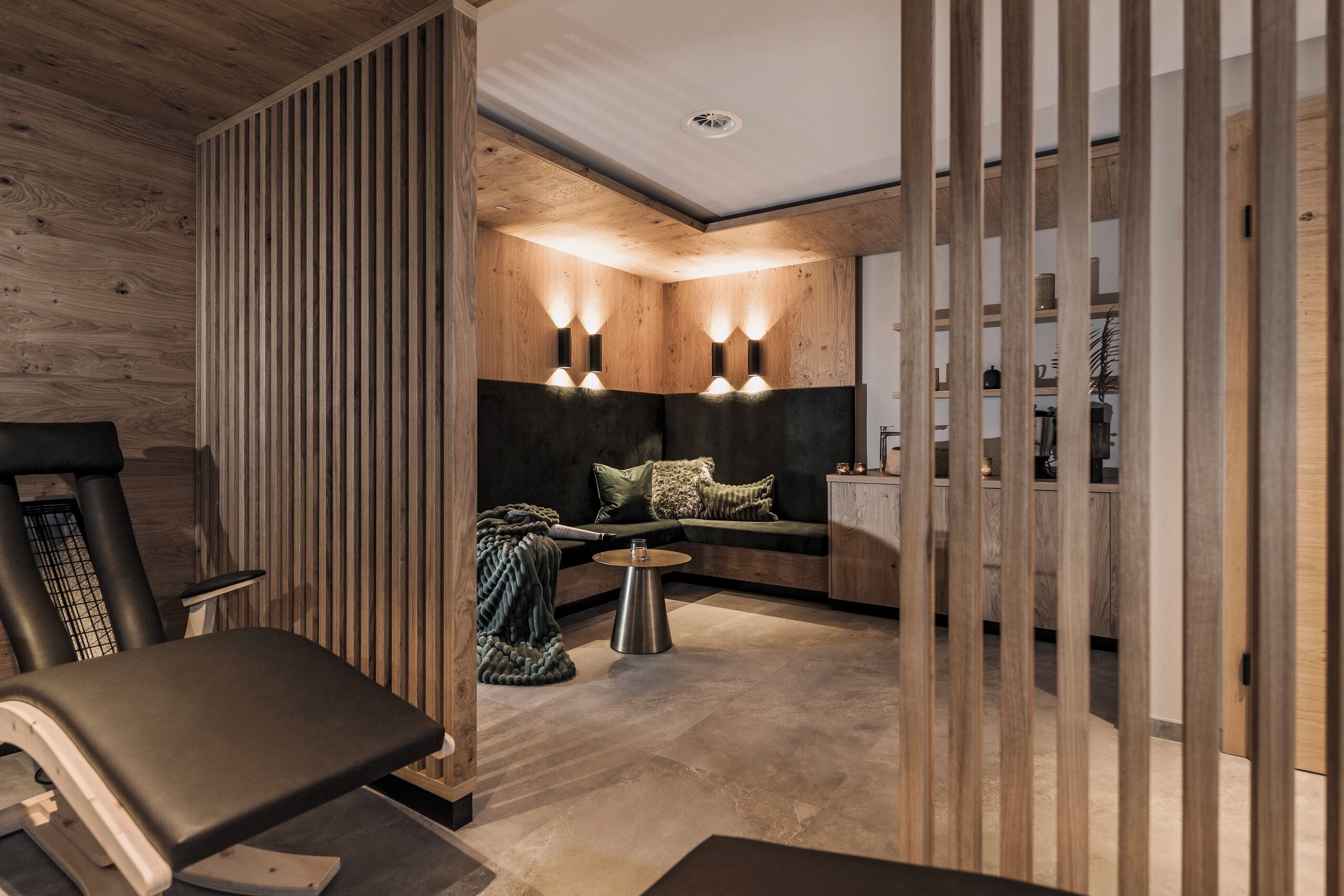 A modern living room with a treadmill, a dark-colored sofa with cushions, a round coffee table, and wooden paneling on the walls.