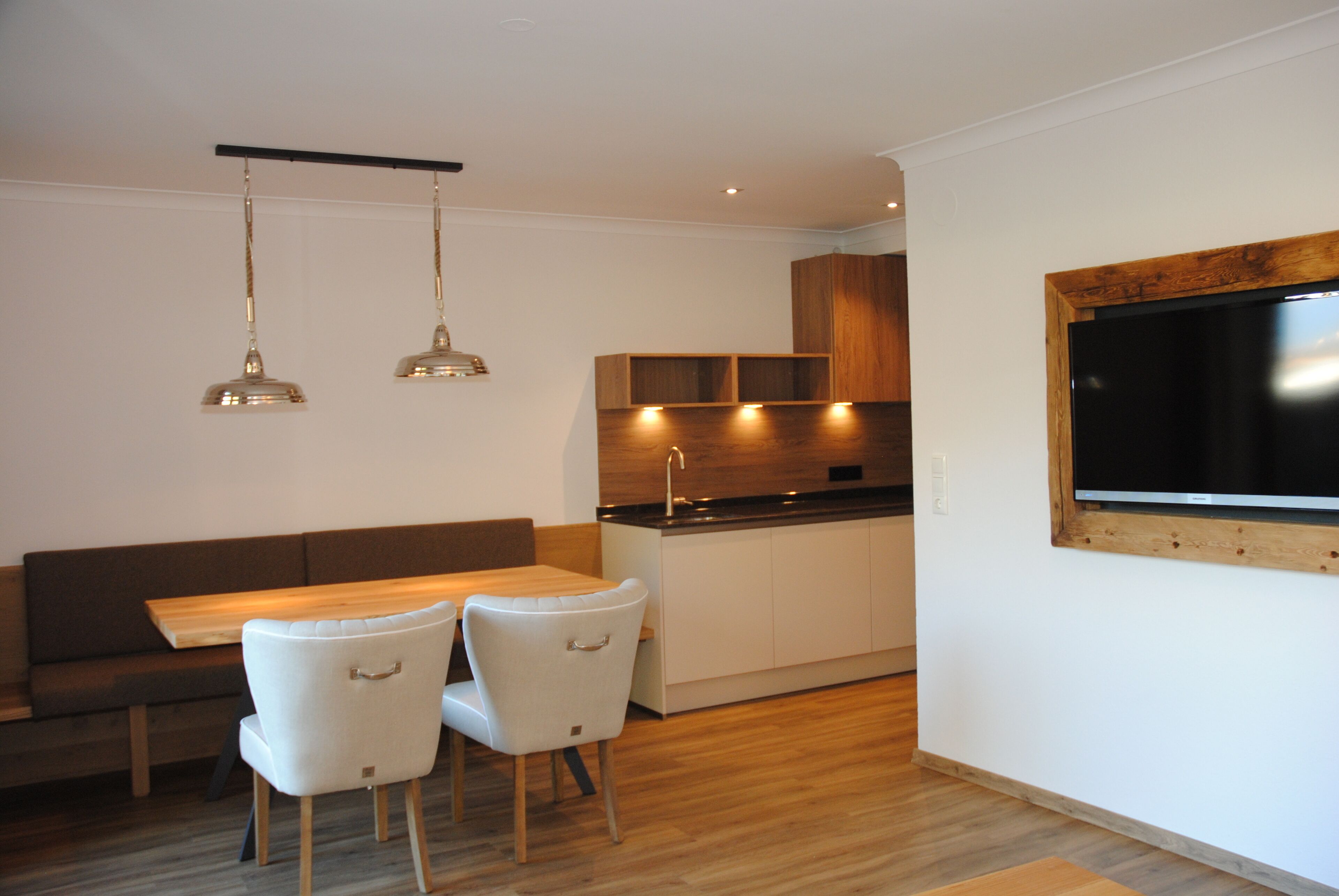 Una cocina moderna con armarios de madera, horno empotrado y comedor con mesa de madera y dos sillas.