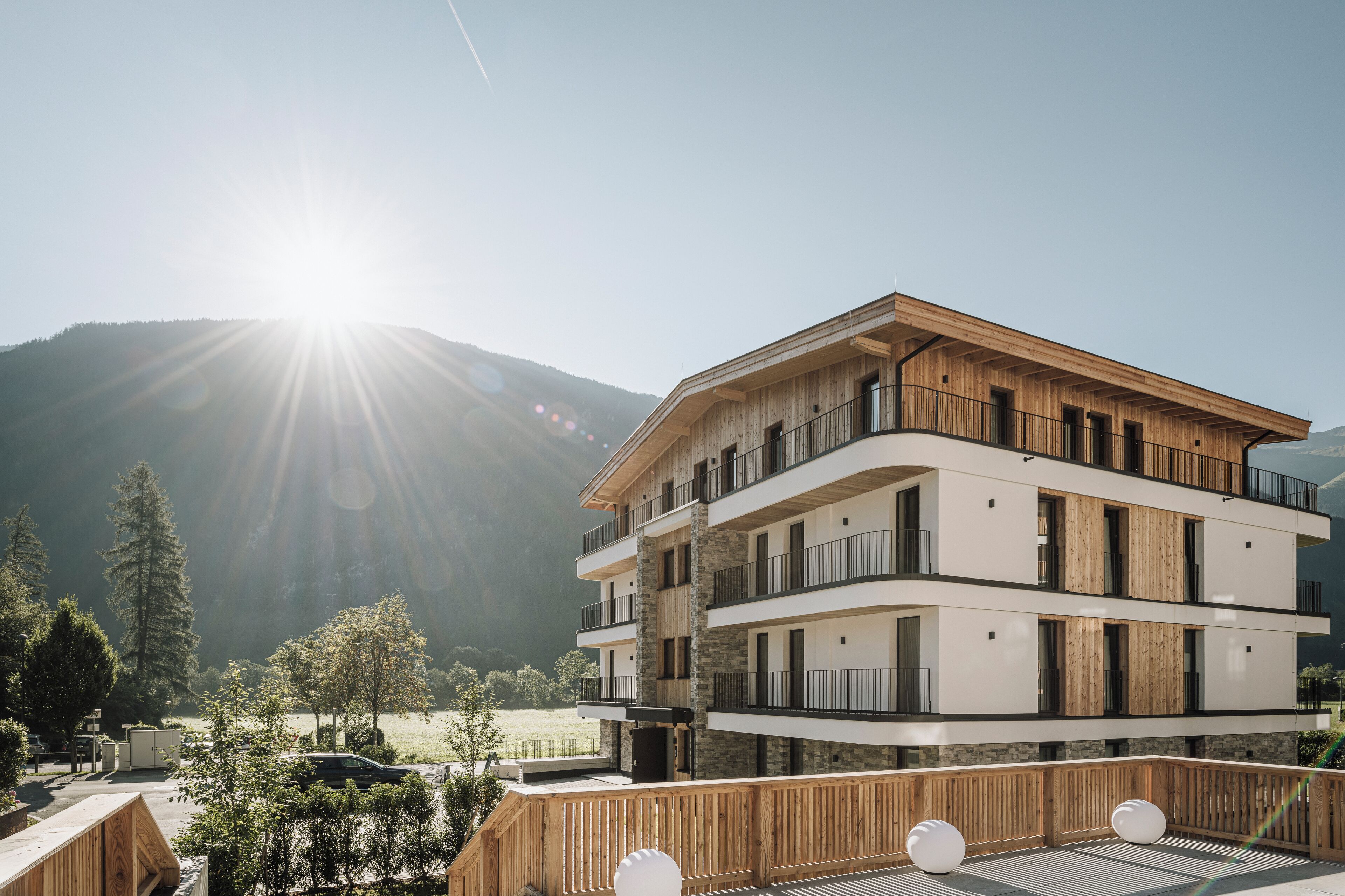 Un edificio a più piani con balconi, facciata in legno e montagne sullo sfondo.