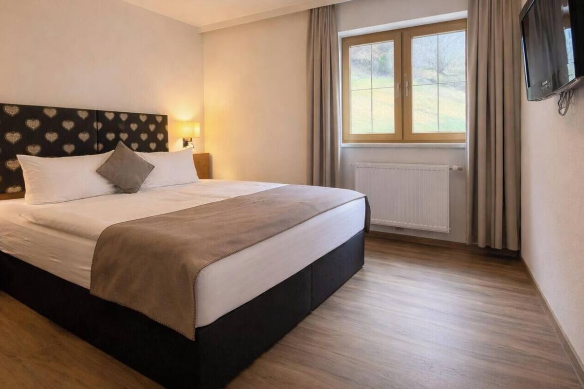 Une chambre d’hôtel avec un lit, des lampes de chevet, une fenêtre avec des rideaux et un téléviseur fixé au mur.
