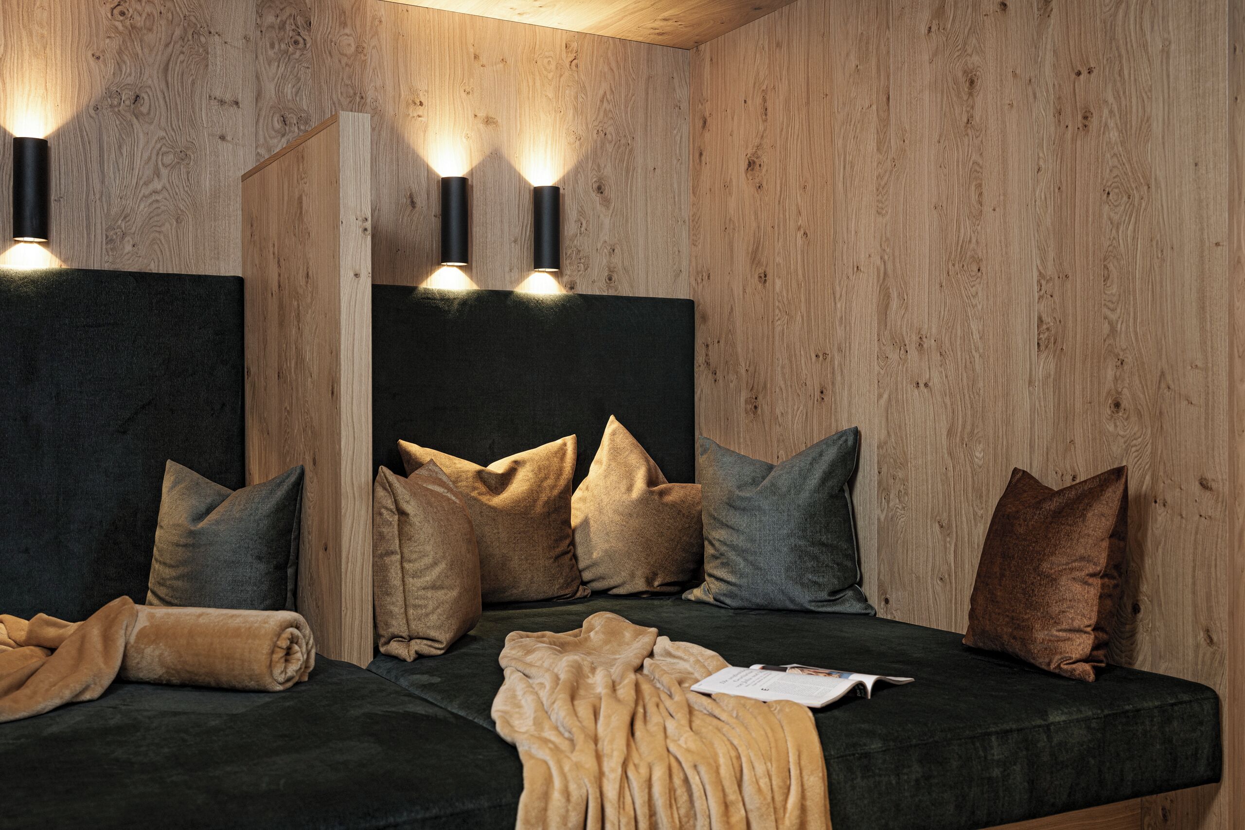 A modern room with a dark green sofa, multiple pillows, and a wooden wall.
